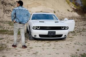 costas do homem dentro jeans Jaqueta e boné perto dele branco músculo carro dentro carreira. los angeles. foto