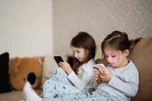 dois irmãs vestem pijamas jogando telefones cedo dentro manhã. foto