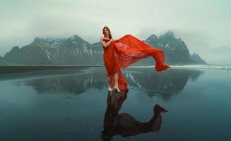 ruiva modelo dentro vermelho vestir em Reynisfjara de praia cênico fotografia foto