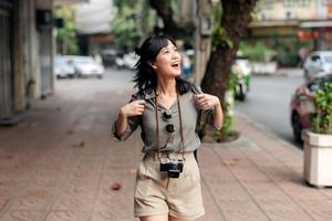 jovem ásia mulher mochila viajante desfrutando rua cultural local Lugar, colocar e sorriso. viajante verificação Fora lado ruas. foto