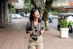 jovem ásia mulher mochila viajante desfrutando rua cultural local Lugar, colocar e sorriso. viajante verificação Fora lado ruas. foto