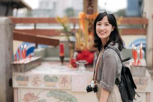 jovem ásia mulher mochila viajante desfrutando rua cultural local Lugar, colocar e sorriso. viajante verificação Fora lado ruas. foto