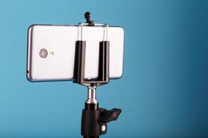 smartphone em um tripé como uma câmera de foto e vídeo em um fundo azul. gravar vídeos e fotos para o seu blog.