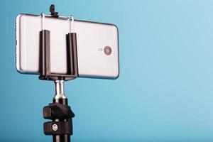 smartphone em um tripé como uma câmera de foto e vídeo em um fundo azul. gravar vídeos e fotos para o seu blog.
