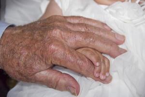 mãos de velho aposentado segurando um recém-nascido foto