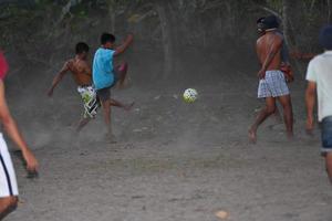 Gili Asahan, Indonésia - 22 de agosto de 2016 - meninos estão jogando futebol ao pôr do sol em um campo de palmeiras perto da praia foto