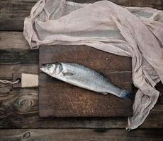 peixe robalo inteiro fresco na tábua de corte marrom foto