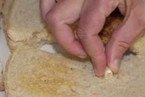 fêmea mão enquanto espalhando alho em pão dentro italiano cozinha foto