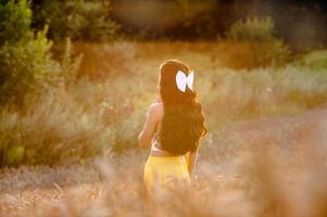 uma menina dentro uma amarelo saia carrinhos dentro uma campo contra a fundo do a configuração Sol foto