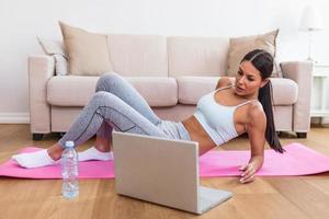 jovem mulher exercício às casa dentro uma vivo sala. vídeo lição. jovem mulher recorrente exercícios enquanto assistindo conectados exercite-se sessão. lindo jovem mulher fazendo ginástica exercício às casa foto