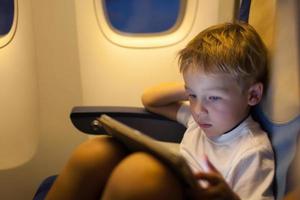 menino sentado em um avião usando um tablet foto