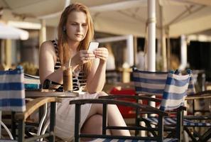 mulher enviando mensagens de texto em seu telefone enquanto está sentada em um café ao ar livre foto