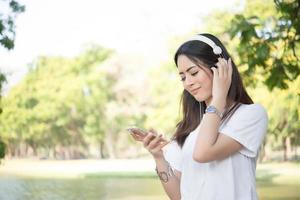 retrato de uma menina sorridente com fones de ouvido ouvindo música na natureza foto