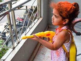 doce pequeno indiano menina jogando cores em holi festival, segurando pichakaree cheio do cores, holi festival celebrações dentro Délhi, Índia foto