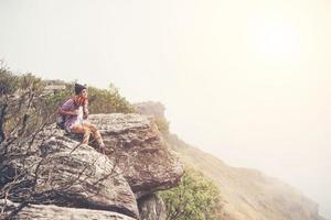 jovem alpinista com mochila sentado à beira de um penhasco foto