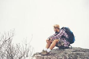 caminhante jovem hippie com mochila sentado no topo da montanha foto