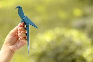 mão segurando um pássaro de origami azul com fundo borrado da natureza foto