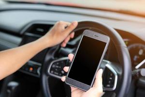 mãos segurando um celular e um volante no interior do carro foto