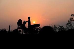 silhueta de criança em ciclomotor com sol baixo no céu foto