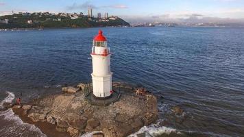 paisagem marinha com um farol próximo a um corpo d'água e céu azul nublado em vladivostok, na Rússia foto