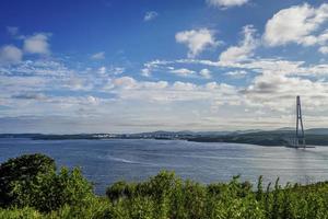 vista do mar de campo verde pela baía do chifre dourado e a ponte zolotoy com céu azul nublado em vladivostok, Rússia foto