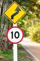 sinal de tráfego de limite de velocidade seletivo 10 e símbolo de advertência de estrada sinuosa para segurança na estrada rural na floresta de montanha, chave baixa foto