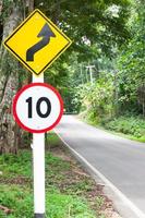 sinal de tráfego de limite de velocidade seletivo 10 e símbolo de advertência de estrada sinuosa para segurança na estrada rural na floresta de montanha, chave baixa foto