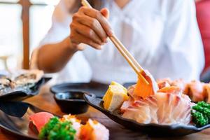 jovem ásia mulher comendo sashimi conjunto dentro japonês restaurante foto