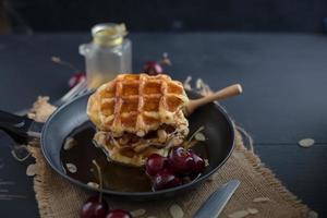 mel em waffles em uma panela com cerejas na mesa de madeira escura foto