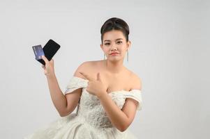 jovem ásia lindo noiva postagem com crédito cartão e Smartphone dentro mão foto