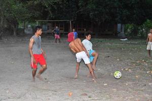 Gili Asahan, Indonésia - 22 de agosto de 2016 - meninos estão jogando futebol ao pôr do sol em um campo de palmeiras perto da praia foto