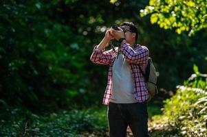 homem jovem mochileiro usa câmera para tirar fotos na floresta.