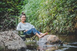 jovem sentada na cadeira de acampamento no riacho para relaxar foto