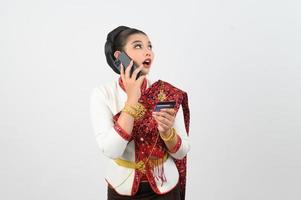 retrato do lindo tailandês mulher dentro tradicional roupas posando com Smartphone e crédito cartão foto
