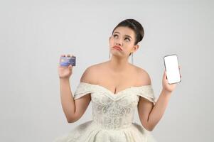 jovem ásia lindo noiva postagem com crédito cartão e Smartphone dentro mão foto