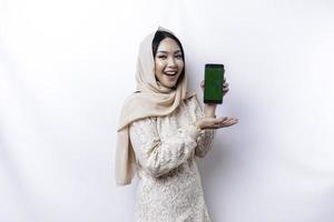 uma retrato do uma feliz ásia muçulmano mulher vestindo uma hijab, mostrando dela telefone tela, isolado de branco fundo foto