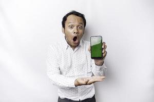 chocado ásia homem vestindo uma branco camisa e mostrando verde tela em dele telefone, isolado de branco fundo foto