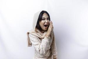 jovem lindo ásia muçulmano mulher vestindo uma hijab gritando e gritando alto com uma mão em dela boca. comunicação conceito. foto