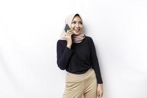 uma retrato do uma feliz ásia muçulmano mulher vestindo uma hijab, segurando dela telefone, isolado de branco fundo foto