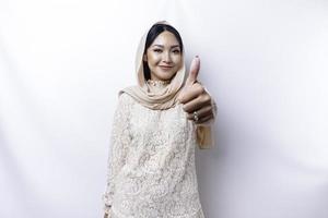 animado ásia muçulmano mulher vestindo uma hijab dá polegares acima mão gesto do aprovação, isolado de branco fundo foto