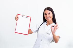 retrato do uma jovem fêmea médico dentro uma laboratório casaco poses com uma prancheta dentro mão mostrando Está bem placa. isolado em branco. foto