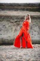 lindo mulher dentro laranja vestir posando às a fundo do areia Colina foto