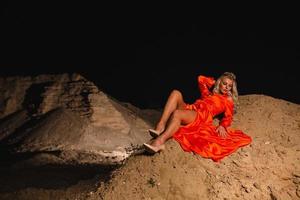 loiro mulher com fino nu pernas dentro laranja vestir sentado em a areia Colina foto
