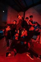 uma grupo do ásia adolescentes dentro Preto roupas posando muito danadinho com seus amigos dentro uma armazém com uma vermelho luz foto