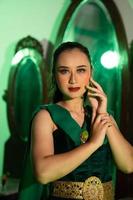 uma fêmea javanese dançarino dentro uma verde dança traje e uma cheio face com Maquiagem poses com dela mãos dentro frente do uma vestir mesa foto