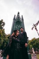 uma casal do ásia adolescentes em pé perto uma assustador cemitério cheio do verde árvores foto