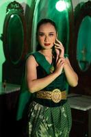 uma fêmea javanese dançarino dentro uma verde dança traje e uma cheio face com Maquiagem poses com dela mãos dentro frente do uma vestir mesa foto