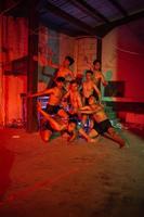 uma grupo do homens sem roupas dançando poses dentro a velho construção com uma vermelho luz foto