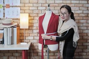 designer de moda feminina madura asiática fica perto de vestir o fantoche, olhando para a câmera com um sorriso no estúdio, orgulhosamente trabalha com coleção de design de roupas, empresário de sme de alfaiate profissional.