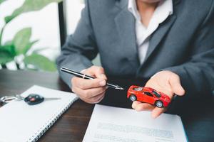 o negócio mulher mão protegendo vermelho brinquedo carro em escrivaninha. planejamento para gerir transporte finança custos. conceito do carro seguro negócios, salvando Comprar - venda com imposto e empréstimo para Novo carro. foto